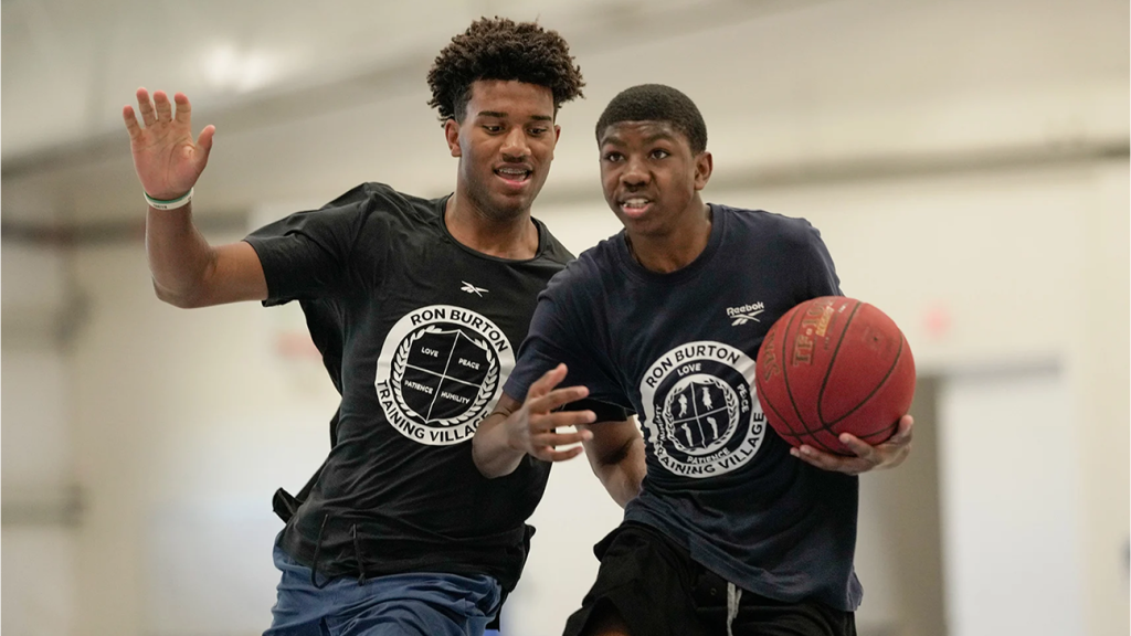 Two teenagers playing basketball indoors in a gym.