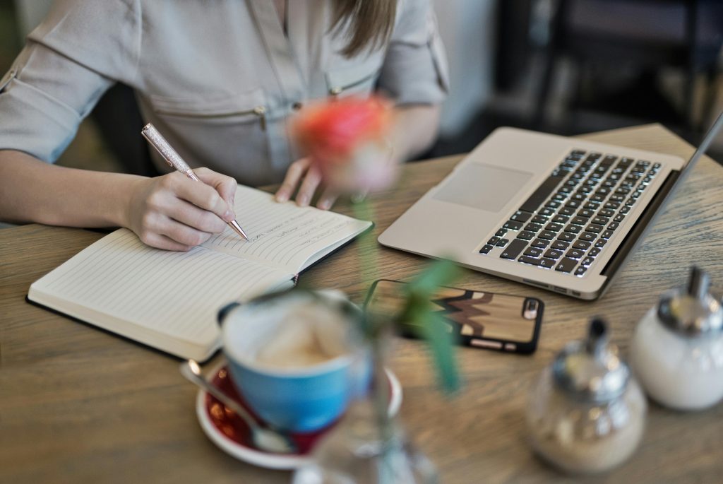A person working on a laptop and writing in a notebook.